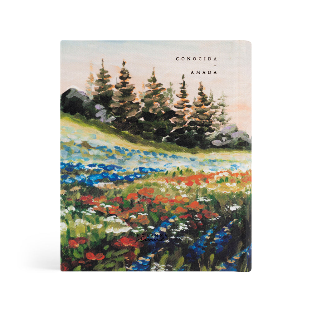 Bible with a scenic cover featuring trees and flowers, labeled 'Conocida y Amada'.