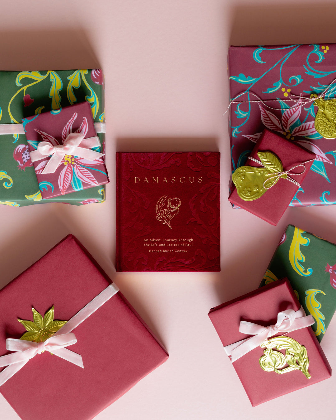A flat-lay arrangement of wrapped gift boxes and a central red box labeled DAMASCUS, styled on a soft pink background.
