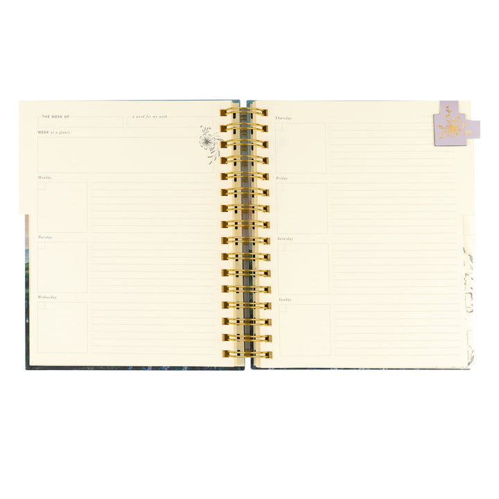 Open spiral-bound planner with gold binding on a white background