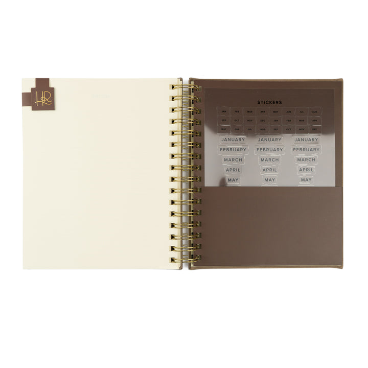 Open spiral-bound planner with a page of stickers on a white background