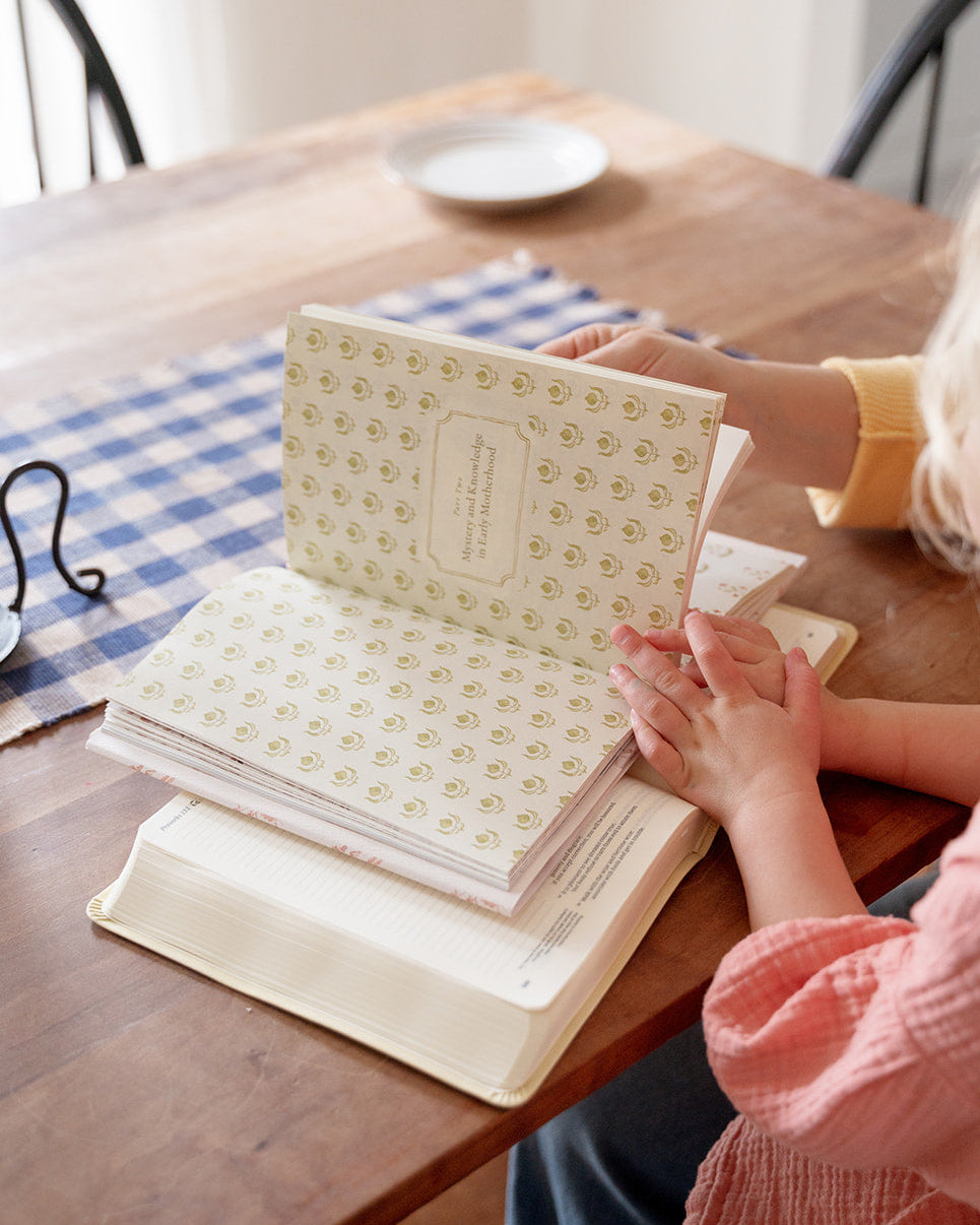 Two children sitting at a wooden table with an open book in front of them.