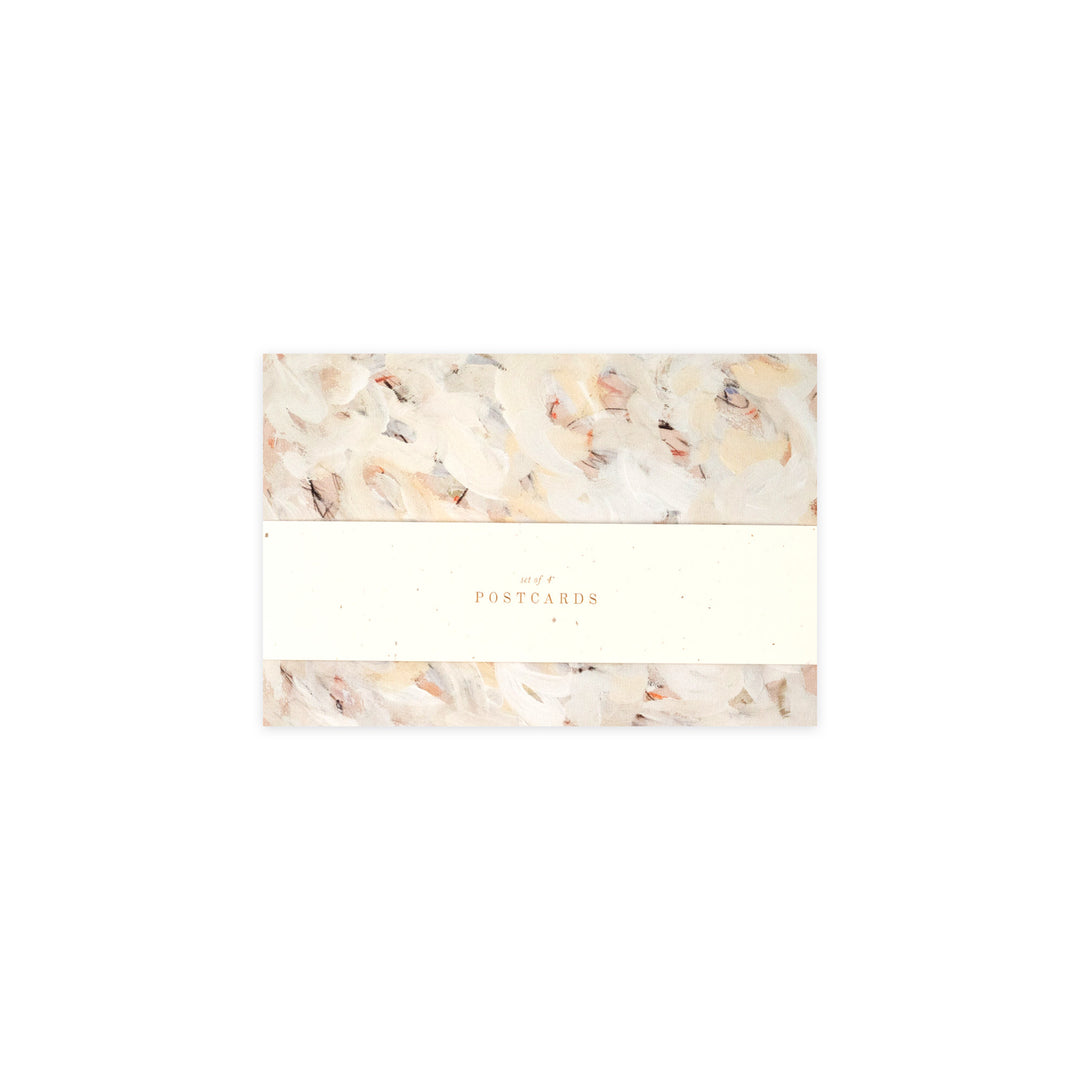 A pack of postcards wrapped in a cream paper band with the word 'POSTCARDS' printed in gold, set against a clean white background.