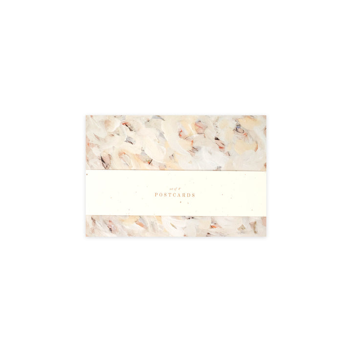 A pack of postcards wrapped in a cream paper band with the word 'POSTCARDS' printed in gold, set against a clean white background.